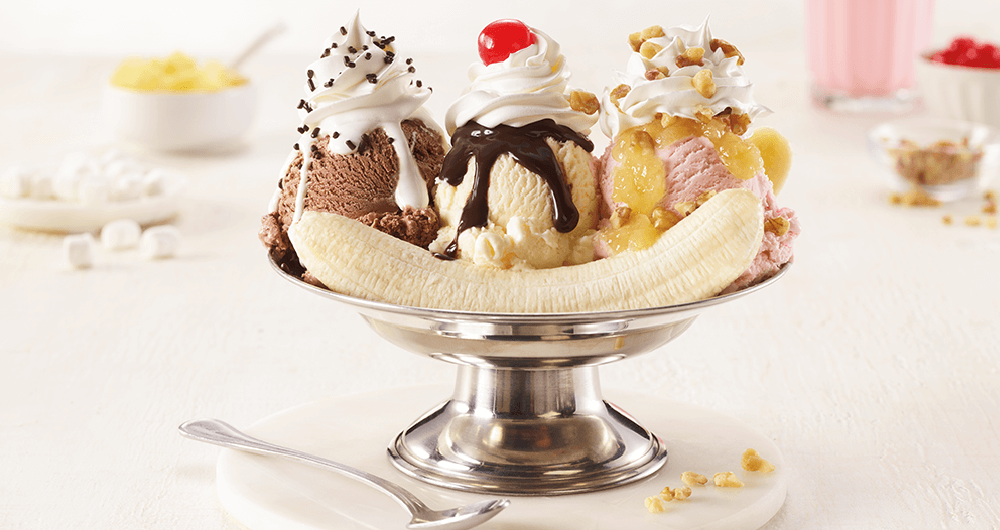 Banana split with one scoop chocolate, one scoop vanilla, ane one scoop strawberry with chocolate syrup, sprinkles and whipped cream in a glass